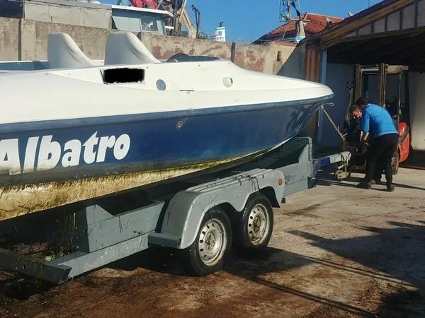 Motoscafo offshore con livrea bianca e blu sbiadita, sul carrello prima dell'intervento
